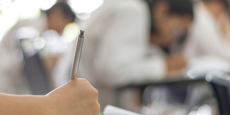 Applicant hand holding pen writing doing examination with blurred abstract background other applicants attending exam classroom