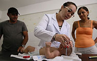 In Brazil, in a clinic, medical worker measures a baby’s head circumference while mother and father look on