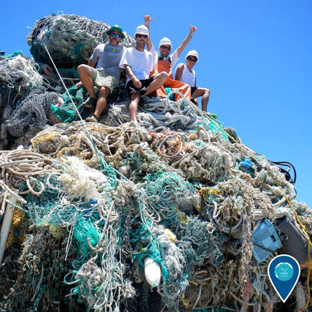 photo of 4 people standing on a pile of nets and ropes that are marine debris