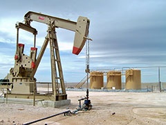 Well pad showing pump jack with storage tanks in the background