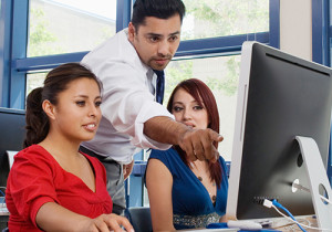 A photograph of a mentor educating two students in front of a computer monitor.