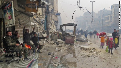 Syrian pro-regime fighters gesture as residents, fleeing violence in the restive Bustan al-Qasr neighbourhood, arrive in Aleppo&#39;s Fardos neighbourhood on December 13, 2016, after regime troops retook the area from rebel fighters. 
Syrian rebels withdrew from six more neighbourhoods in their one-time bastion of east Aleppo in the face of advancing government troops, the Syrian Observatory for Human Rights said. / AFP / STRINGER        (Photo credit should read STRINGER/AFP/Getty Images)