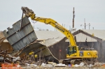 A heavy equipment operator uses a shear to move a large section of wall from the C-746-B warehouse during demolition.