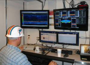 Acoustics team leader Warren Mitchell examines sonar display. Miami Dolphins “thinking cap”: optional.