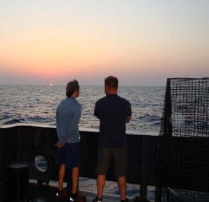 Todd Kellison (l) and Warren Mitchell (r) confer at sunrise as their long night’s acoustics lab work continues past dawn. Photo credit: David Berrane