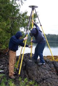 Researchers are kneeling in a sitka spruce forest as they check the computer that is collects and records tidal data on a small island in Nossuk Bay, Alaska.