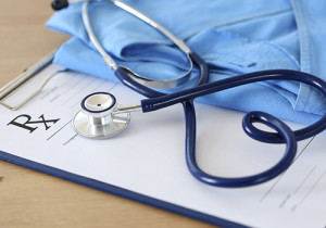 Prescription form clipped to pad lying on table with stethoscope twisted in heart shape and blue doctor uniform closeup. Medicine or pharmacy concept. Empty medical form ready to be used