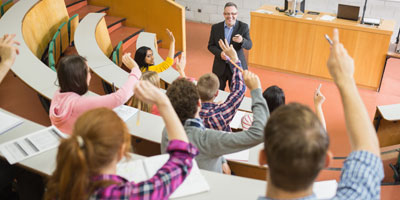 Postsecondary students raising their hands in lecture hall