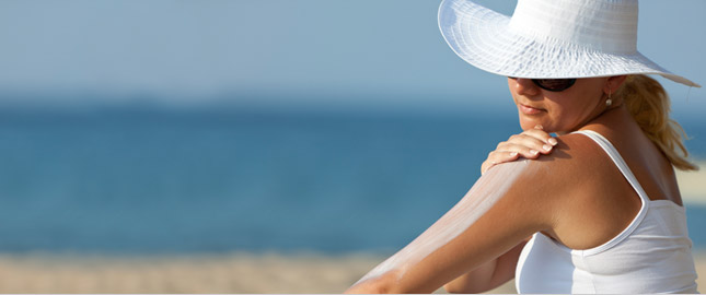 A woman wearing protective clothing at the beach putting sunscreen on her arm