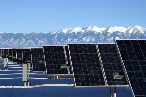 Photo of several rows of large solar modules with the Rocky Mountains in the background