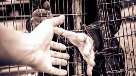 Man reaches toward outstretched hand at a gate to provide assistance to a potential victim of human trafficking. [Shutterstock Photo]