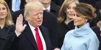 President Trump with one hand raised and one on bible being held by Melania Trump (© AP Images)