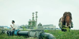 A man sitting on a large pipe with an elephant standing nearby (Sundance Institute/Photo by Chananun Chotrungroj)