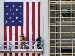 Workers on scaffolding erecting large flag (© AP Images)