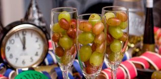 Trois flûtes à champagne remplies de grains de raisin avec un réveil à minuit moins cinq en arrière-plan (© AP Images)