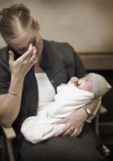 Photograph of a woman, looking upset, holding a baby