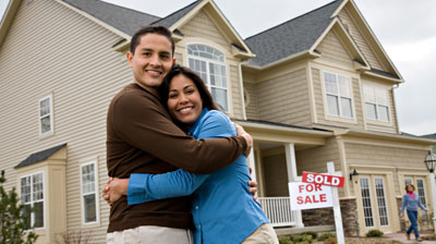 Happy couple in front of house with sold sign