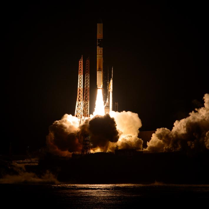 The Japanese H-IIA rocket launching over the water, with flames and smoke