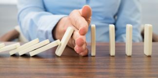 Une main empêchant des dominos alignés de continuer de tomber (Shutterstock)