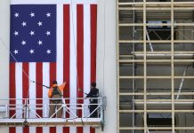 Trabalhadores em andaime erguendo uma grande bandeira (© AP Images)