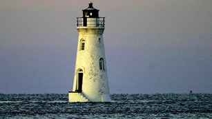 Cockspur Lighthouse standing in the ocean with the water level reaching its base