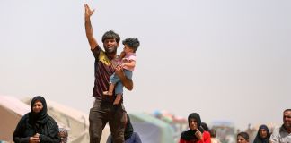 Un hombre con un niño en brazos levanta la mano (© AP Images)