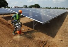 Worker in hard hat operating power tamper next to solar panel array (© AP Images)