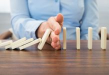 Tangan menghentikan domino agar tidak roboh (Shutterstock)