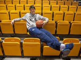 Man sitting on yellow bleacher seats holding basketball (State Dept./D.A. Peterson)