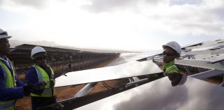 Three men holding solar panel (© AP Images)