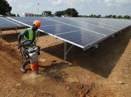 Trabalhador com capacete de proteção trabalha próximo de painéis solares (© AP Images)