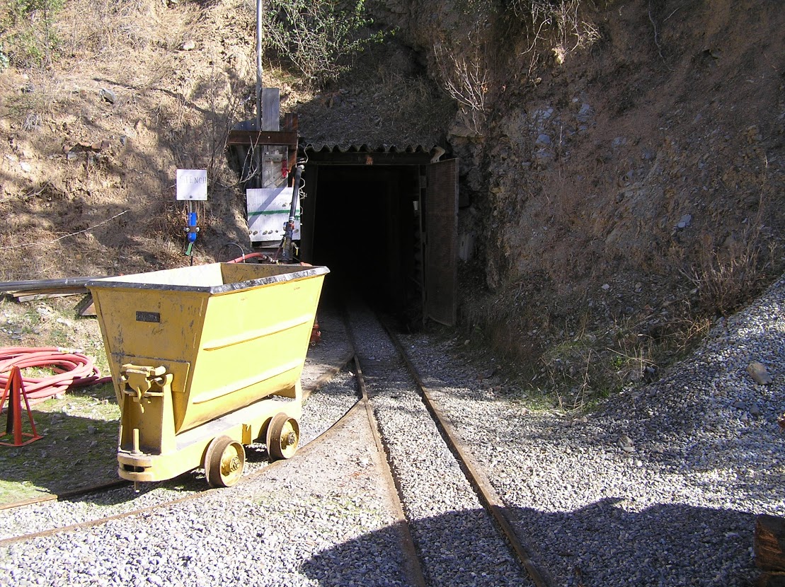 A small rail car sits on the rails leading into a mine.