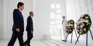 Two men walking toward wreaths of flowers attended by man in uniform (© AP Images)