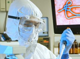 Scientist in full protection suit in lab with image of Ebola virus onscreen (© AP Images)