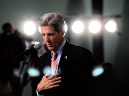 John Kerry speaking, with bright lights behind him (© AP Images)