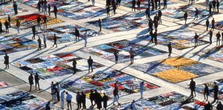 Des gens en train de marcher autour de panneaux de tissus décorés, étalés par terre (© AP Images)