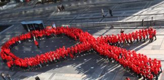 Grupo de pessoas reunidas formam um laço vermelho (Depto. de Estado)