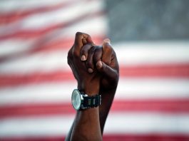 Two clasped African-American hands raised in front of American flag (© AP Images)