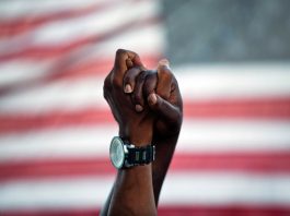 Duas mãos afro-americanas unidas levantadas na frente da bandeira americana (© AP Images)