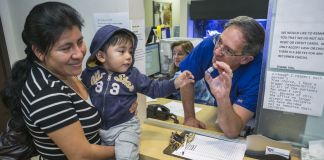 Doctor holding vaccine vial in front of mother holding child (© AP Images)