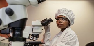 Mujer con uniforme hospitalario frente a un microscopio (Foto cedida por el Instituto Africano para la Investigación del VIH y la tuberculosis KwaZulu-Natal).