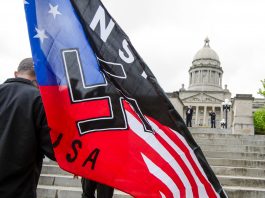 Un homme tenant un drapeau avec la croix gammée devant un capitole (© AP Images