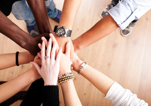 A group of diverse people join hands in cooperation.