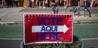 People standing in line and sign saying 'Vote Here' (© AP Images)