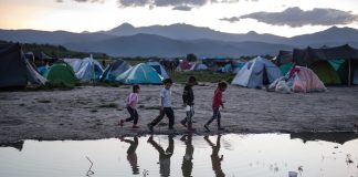 Children standing near tents and puddle of water (© AP Images)