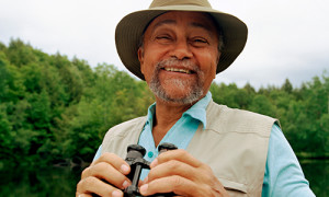 A smiling older man outside holding binoculars 