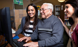An older man and his two granddaughters use the computer in a library