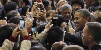 Smiling President Obama surrounded by people taking pictures (© AP Images)