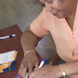 A woman filling out paperwork with a pill bottle on the desk.