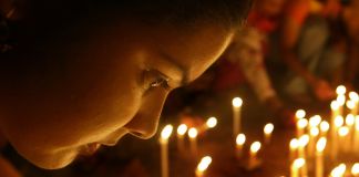 Woman looking at many lit candles during vigil (© AP Images)